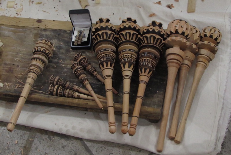Photograph of eleven different molinillos being made in a workshop.